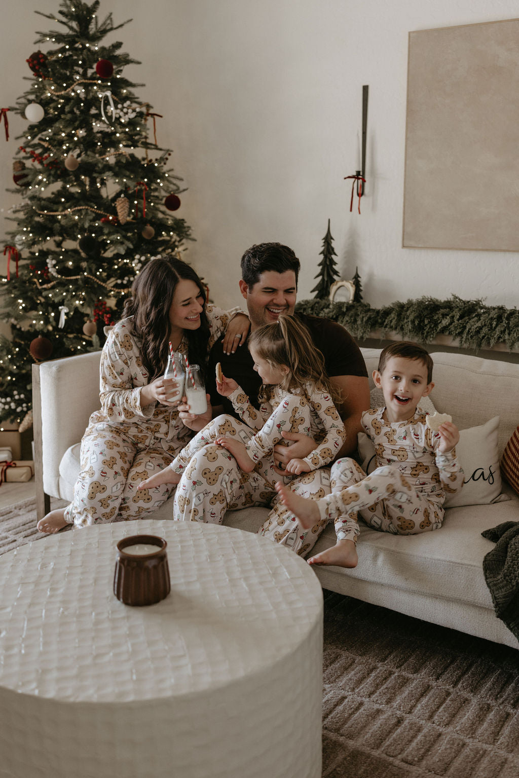 Family sitting on a couch in front of a decorated Christmas tree, all wearing matching pajamas.
